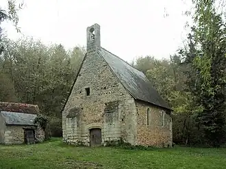 Photographie en couleurs d'un petit édifice religieux sur une pelouse entouré de bois.