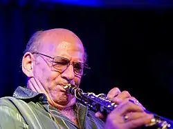 photo d'un homme chauve à lunettes en trian de jouer du saxophone