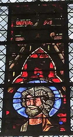 Vitrail avec des teintes dominantes rouges et bleues représentant, en sa partie inférieure, un homme barbu pourvu d'une auréole.