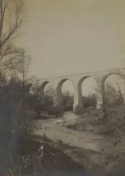 Photographie en sépia d'un cours d'eau serpentant et passant sous l'arche du pont.