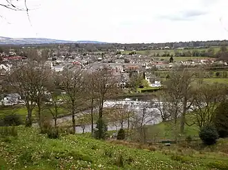 Photographie couleur d'un village situé le long d'une rivière, vus depuis une colline.