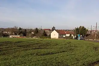 Vue d'un hameau en second plan ; zone agricole au premier plan.