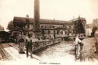 Vue d'une usine et de sa cheminée au bord d'un cours d'eau sur une carte postale des années 1900.