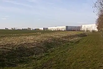 Vue d'une parcelle agricole plate et d'entrepôts à l'arrière plan.