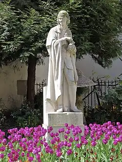 Statue de Voltaire entourée de fleurs.