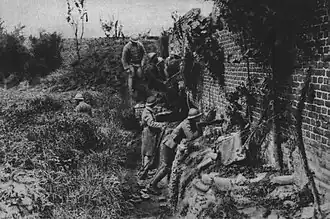 Pendant la Grande Guerre, près de Chaulnes, des soldats français en poste avancé, protégés derrière un mur, attendent l'ennemi tout proche.
