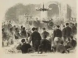 Gravure montrant des hommes attablés écoutant un orateur barbu.