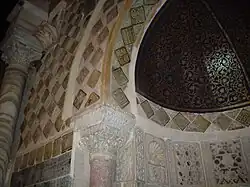Vue partielle de la partie supérieure du mihrab, montrant la demi-coupole peinte, réalisée en bois cintré, de la niche, ainsi que les carreaux lustrés ornant l'intérieur et l'encadrement de celle-ci.