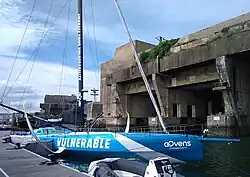 Foiler bleu amarré au ponton, devant l'ancienne base de sous-marins.