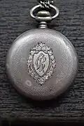 La montre de poche Omega en argent présentée par le Général Berthelot au Père Constantin I. Roșescu, un prêtre orthodoxe roumain et enseignant de Iași, qui devint son ami durant la campagne de la Première Guerre mondiale en Roumanie. La plaque arrière est gravée de "CR", les initiales de Roșescu. Père Roșescu a servi comme confesseur militaire pendant la Première Guerre mondiale, participant aux batailles.
