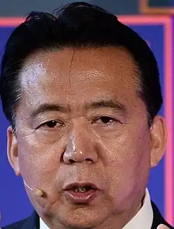 Un asiatique d'une cinquantaine d'années en costume parle. Il porte un casque micro sans fil.