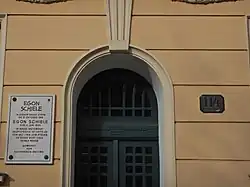 Photo couleur d'une entrée d'immeuble avec une plaque claire et inscriptions en noir