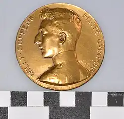 Photographie d'une médaille dorée, représentant un homme de profil. Il est inscrit Willy Coppens - pilote aviateur.