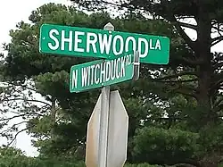 Plaque de rue indiquant « Sherwood La » dans une direction et « N Witchduck Rd » dans l’autre, en lettres blanches sur fond vert.