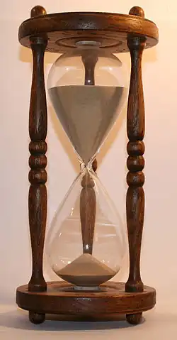 Un sablier en bois à trois colonnes, à moitié rempli de sable.