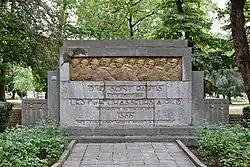 Monument en pierre blanche avec une frise couleur cuivre présentant des soldats en marche cadrés à mi-corps.
