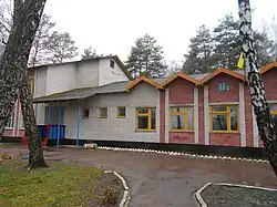 Photographie en couleurs. Bâtiments partiellement colorés. Présence de végétation aux abords. Temps humide, ciel couvert.