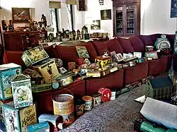 Photo d'un salon avec des meubles, dont un grand canapé à cinq places, couverts de boîtes en fer-blanc de dimensions variées.