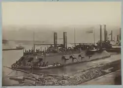 Un navire le long d'un rivage. Le navire possède deux cheminées, arbore le drapeau américain et plusieurs canons sont visibles.