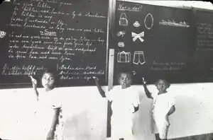 Trois enfants métis prennent la pose devant le tableau noir.